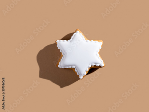 Holiday bakery surprise. Shiny festive pastry. Homemade decorated white icing gingerbread star cookie isolated on beige pastel.