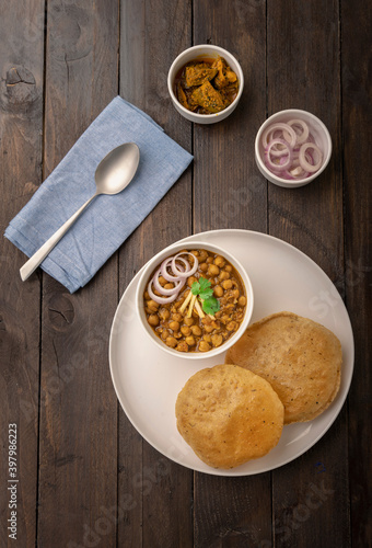 Spicy chick peas curry or Chana Masala or choley with fried puri garnished with sliced onion and green coriander leaf photo