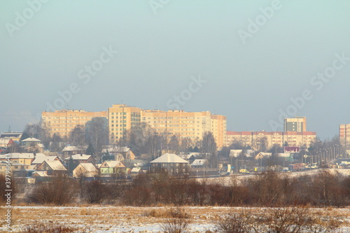 New modern multi-storey houses against the backdrop of small village houses on a clear winter day.