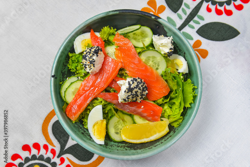 Close up of smoked salmon salad with boiled eggs, cucumbers, cream cheese with sesame seeds and a piece of lemon.