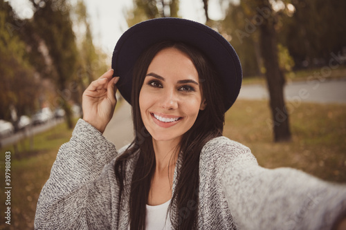 Photo portrait of happy brunette in black hat taking selfie outside smiling wearing grey clothes © deagreez