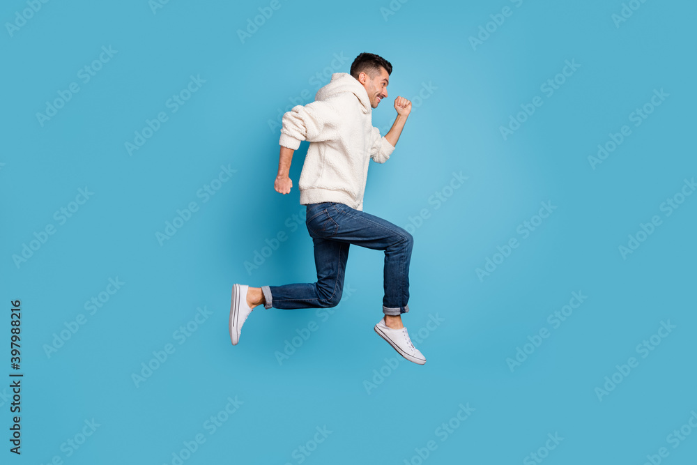 Full size profile sde photo of young happy cheerful positive smiling man jump run isolated on blue color background Full size profile sde photo of young happy cheerful positive smiling man jump run isolated on blue color background