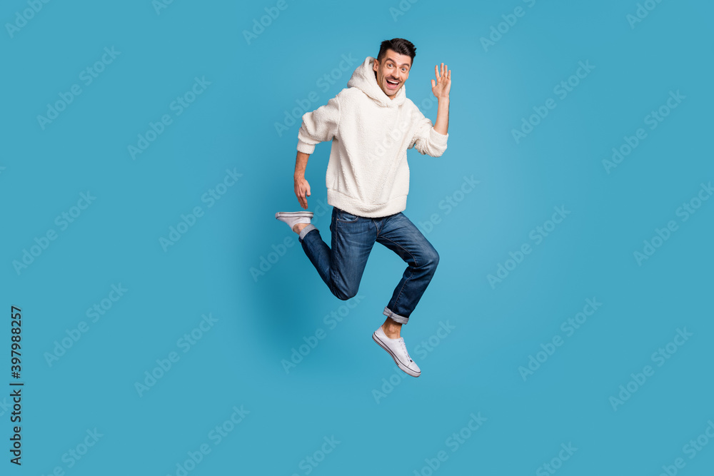 Full size photo of young cheerful positive good mood man smiling jump run say hello isolated on blue color background Full size photo of young cheerful positive good mood man smiling jump run say hello isolated on blue color background