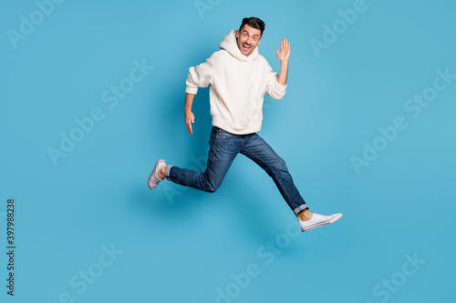 Full size photo of young excited positive happy smiling man jumping running say hi isolated on blue color background