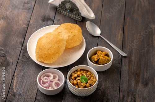 Spicy chick peas curry or Chana Masala or choley with fried puri garnished with sliced onion and green coriander leaf photo