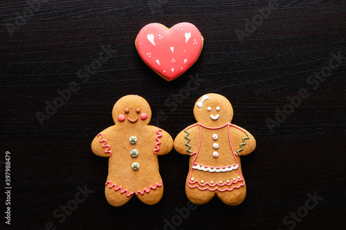 Valentine Day. Festive conceptual background. Romantic relationship. Happy gingerbread man woman cookie couple with red heart in love creative composition on black wooden texture copy space.