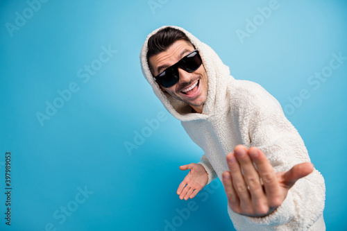 Photo portrait of cool guy in black glasses telling you to come here showing blank space wearing wool hoodie isolated on pastel blue colored background photo