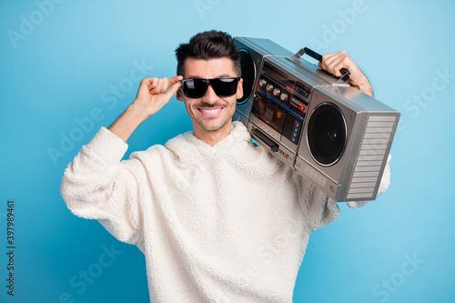 Photo portrait of cool guy with stubble touching glasses carrying boombox on shoulder isolated on pastel blue colored background