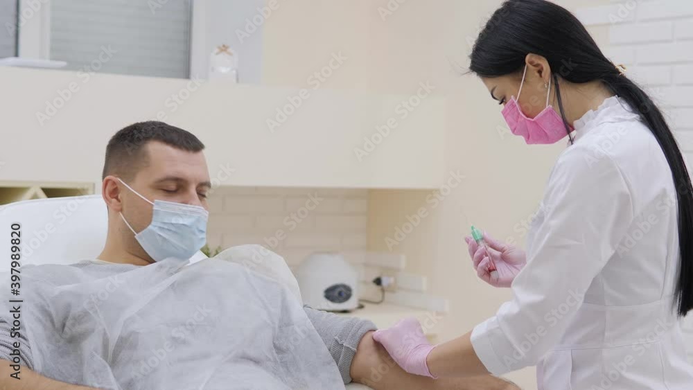 Young female doctor injecting male patient with syringe to collect blood sample in clinic Young female doctor injecting male patient with syringe to collect blood sample in clinic