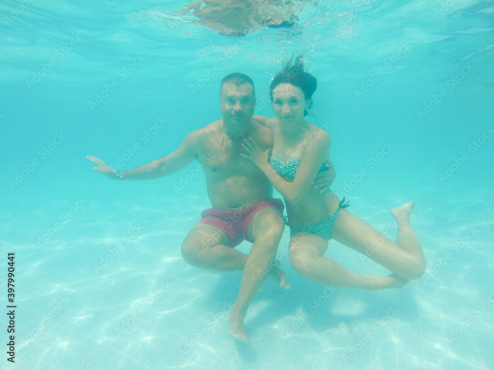 Young woman and man hugging underwater in pool with blue transparent water
