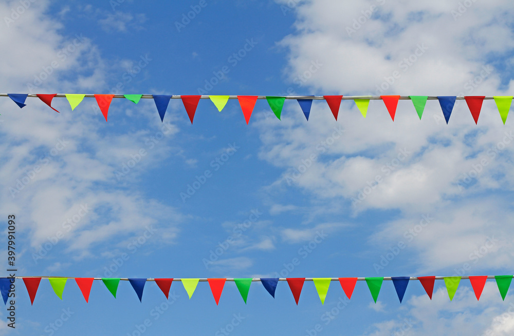 Colorful triangular flags hanging on the blue sky with clouds Colorful triangular flags hanging on the blue sky with clouds