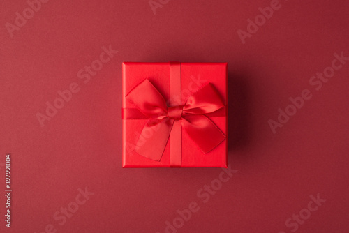 Flat lay layout close up view photo of small present box with bow and ribbon isolated maroon color background