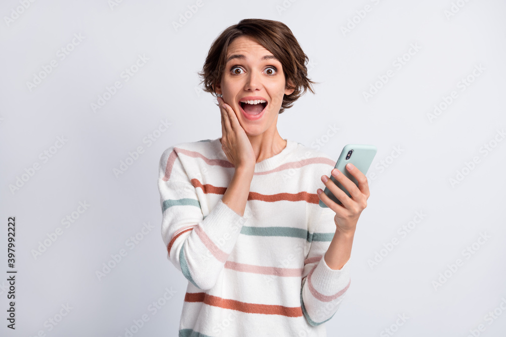 Photo of impressed sweet woman dressed striped pullover holding modern device arm cheek isolated grey color background Photo of impressed sweet woman dressed striped pullover holding modern device arm cheek isolated grey color background
