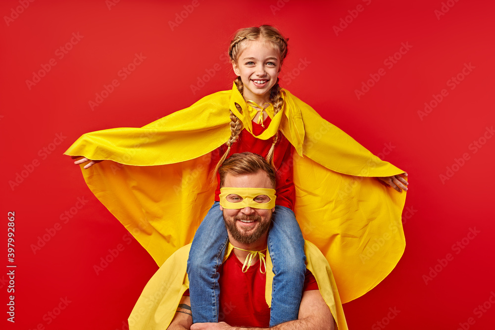 Fototapeta premium kid girl on dad's neck, play superhero game, imitate flight, smile. happy parent and daughter in supehero costumes posing at camera, smile