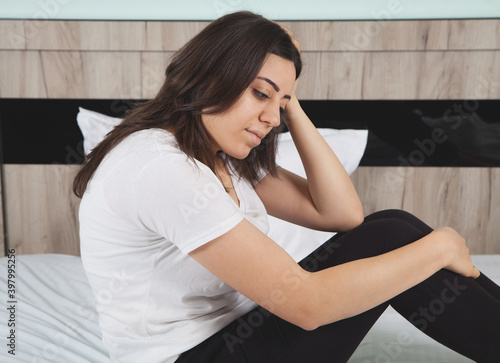 Upset sad woman suffering from in bed. Woman sitting on a bed looking sad.