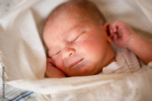 Newborn baby for the first time at home, lying in a blanket on the bed, smiling, yawning, pulling pens, falling asleep, baby's morning, baby products concept.