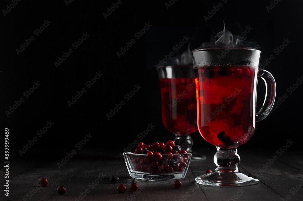 Christmas bright red mulled wine with berries, steam, ripe cowberry, blueberry in two glass wine glasses on black wood table in dark interior, copy space.. Christmas bright red mulled wine with berries, steam, ripe cowberry, blueberry in two glass wine glasses on black wood table in dark interior, copy space..