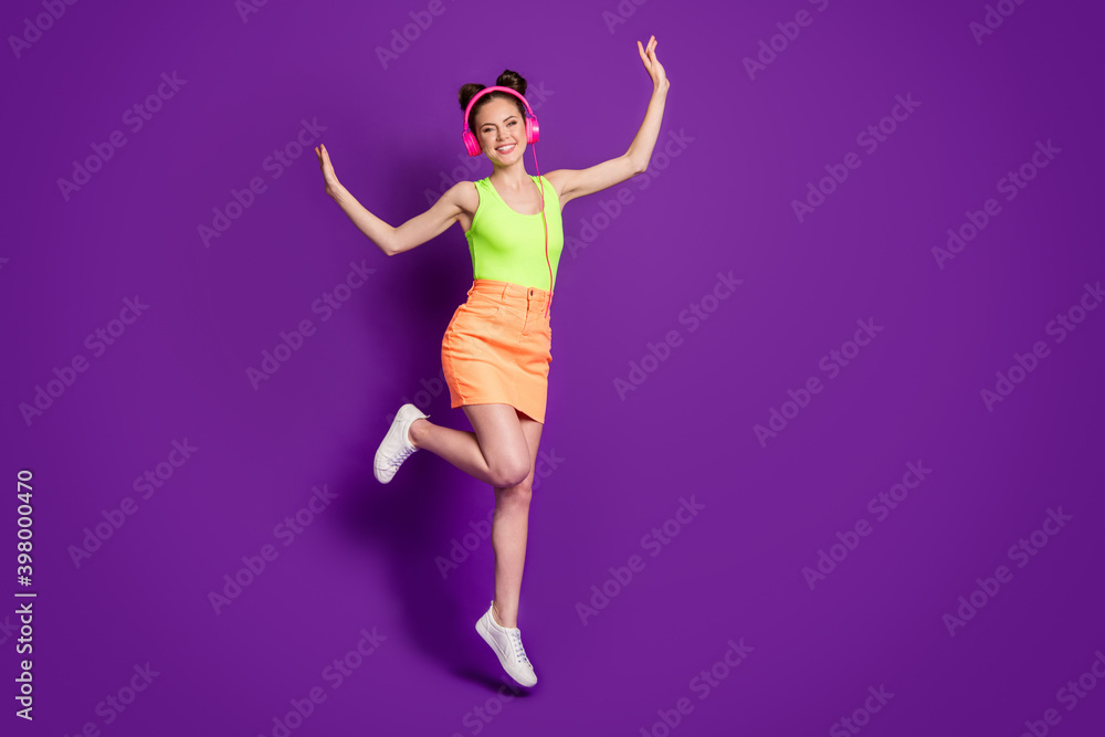 Full length body size view of attractive slim careless cheerful girl jumping listening bass having fun isolated over bright violet color background Full length body size view of attractive slim careless cheerful girl jumping listening bass having fun isolated over bright violet color background