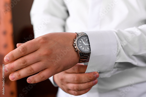Groom's morning, details and husband's meeting on the wedding day. The man fastens a button on the sleeve of his shirt.