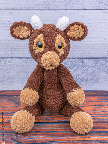 Plush bull toy on a wooden background. Soft toy with lowered legs. Symbol of 2021 New Year.