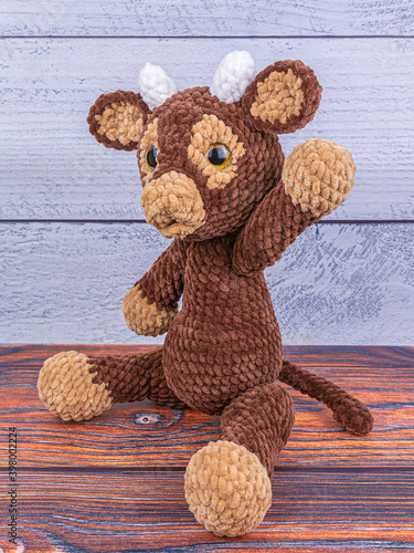 Plush bull toy on a wooden background. A soft toy greets the viewer. Symbol of 2021 New Year.