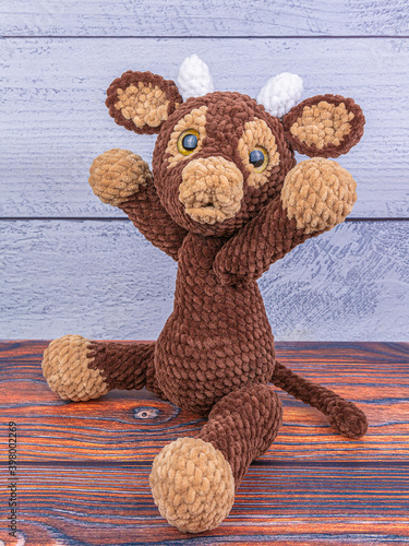 Plush bull toy on a wooden background. A soft toy with elongated lamps. Symbol of 2021 New Year.