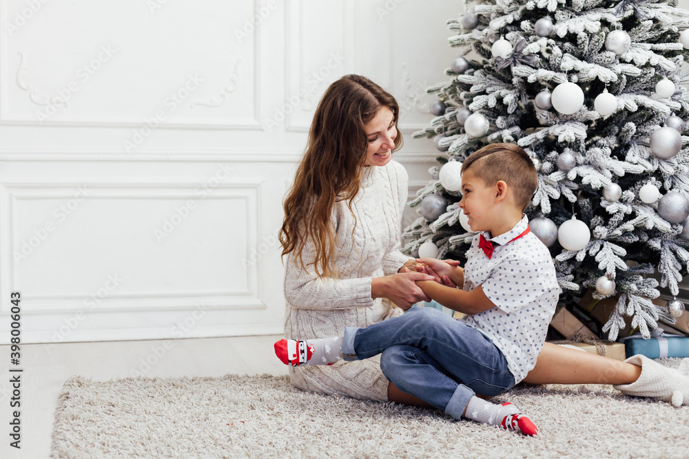 Mom and son sit by Christmas tree presents lights garland new year Mom and son sit by Christmas tree presents lights garland new year