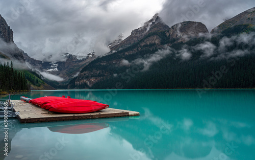 Red canoes on a jetty next to a glacial lake surrounded by mountains in British Columbia, Canada.