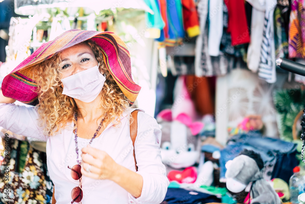 Portrait of a smiling woman blonde and curly haired enjoying the flea market with a beautiful handicraft multi colored hat - one mature woman trendy and happy Portrait of a smiling woman blonde and curly haired enjoying the flea market with a beautiful handicraft multi colored hat - one mature woman trendy and happy