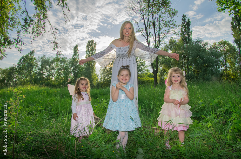 A kind sorceress and little girls elves with wings on a green lawn in the sunlight. Selective focus. Blurred background. A kind sorceress and little girls elves with wings on a green lawn in the sunlight. Selective focus. Blurred background.