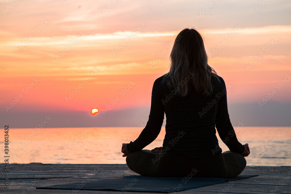 middle-aged woman is meditating at lotus asana at sunrise on the beac
