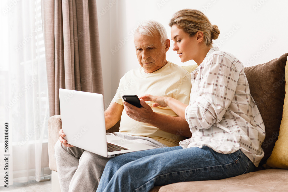 Woman explaining to elderly man how to use laptop and smatphone