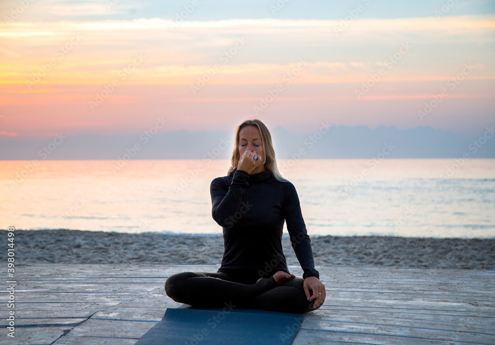 middle-aged woman doing yoga breathing gymnastics at sunrise on the b