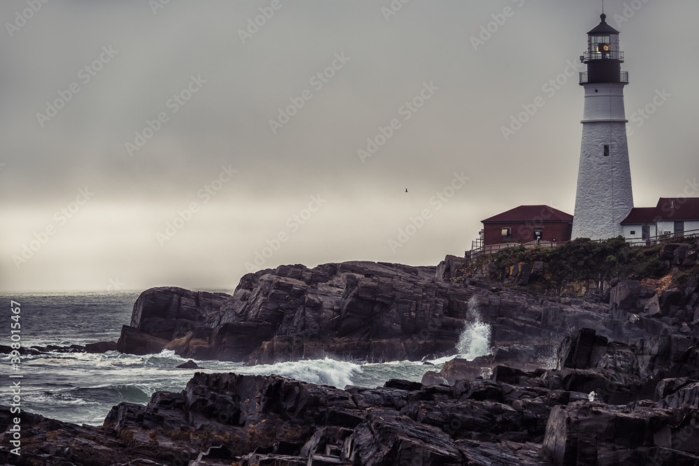 Gloomy dramatic Atlantic coastline. Lighthouse on the rocks and waves breaking on the rocks. Famous lighthouse. Portland. USA. Maine