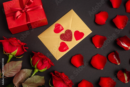 top view of roses, valentines gift and envelope isolated on black