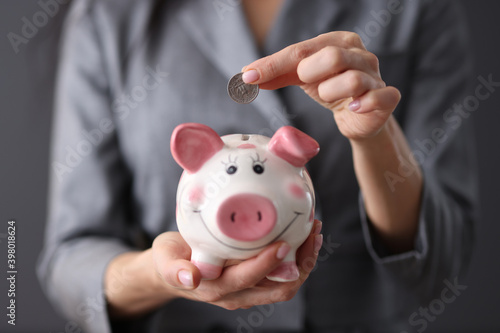 Female hand holds piggy bank and throws coin into it.