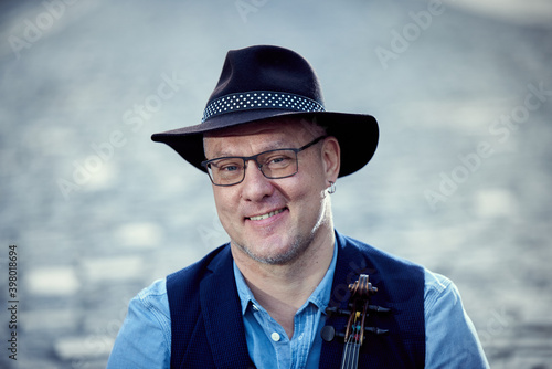 Portrait of a musician man in a hat with a violin on a cobbled road in the city.