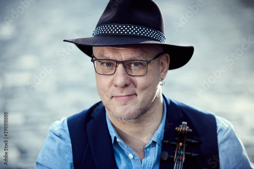 Portrait of a musician man in a hat with a violin on a cobbled road in the city.