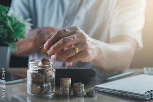 Man's hand taking the coin put in a glass jar, coin pile, calculator, money-saving concept