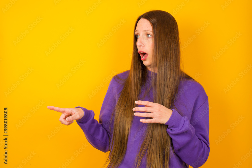 Φωτογραφία Stunned Young beautiful Caucasian woman wearing purple sweater against yellow wa