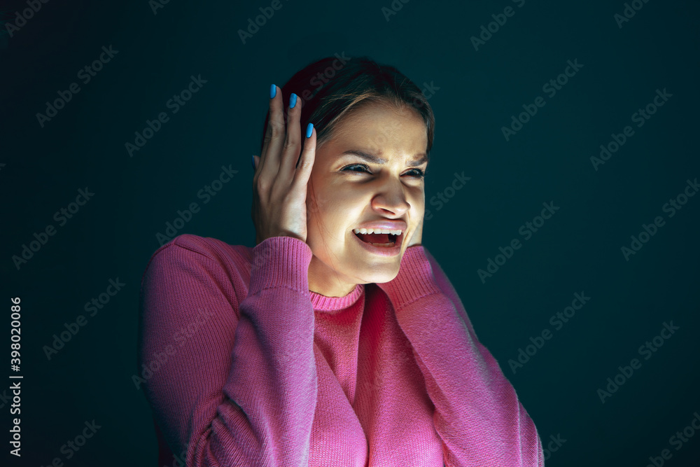 Closing ears. Portrait of young crazy scared and shocked caucasian woman isolated on dark background. Copyspace for ad. Bright facial expression, human emotions concept. Looking horror on TV, cinema. Closing ears. Portrait of young crazy scared and shocked caucasian woman isolated on dark background. Copyspace for ad. Bright facial expression, human emotions concept. Looking horror on TV, cinema.