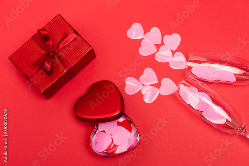top view of pink hearts in champagne glasses near gift box on red background