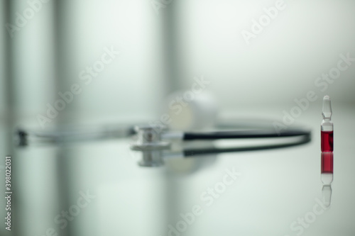 Ampoule with red medicine pills stethoscope on glass table