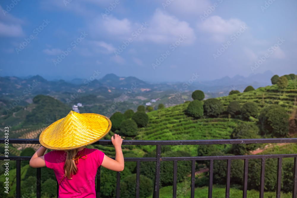 Beautiful closeup of a female leaning on the fences in Asian conical hat against mountains