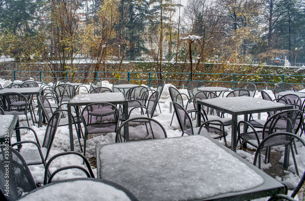 Restaurant chairs and tables covered by snow at the Passer Promenade in Merano, Italy.