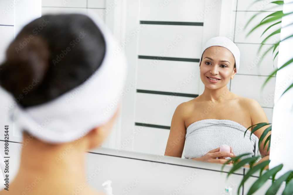 Beautiful woman with deodorant in her hands stands in front of the bathroom mirror Beautiful woman with deodorant in her hands stands in front of the bathroom mirror
