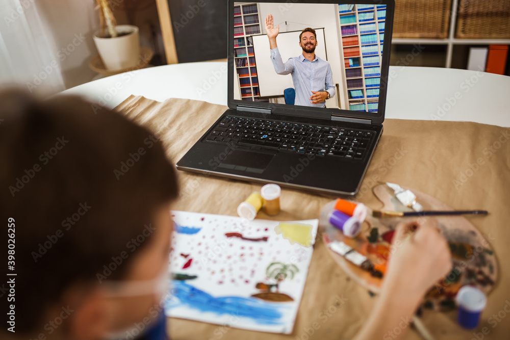 Focused boy painting and watching online course on laptop while practicing at home. Online training, online classes.