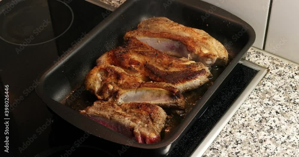 Seasoned pork meat with bone being pan seared in a small tray on an electric stove Seasoned pork meat with bone being pan seared in a small tray on an electric stove