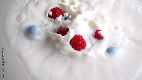 Blueberries and raspberries falling into milk in slow motion