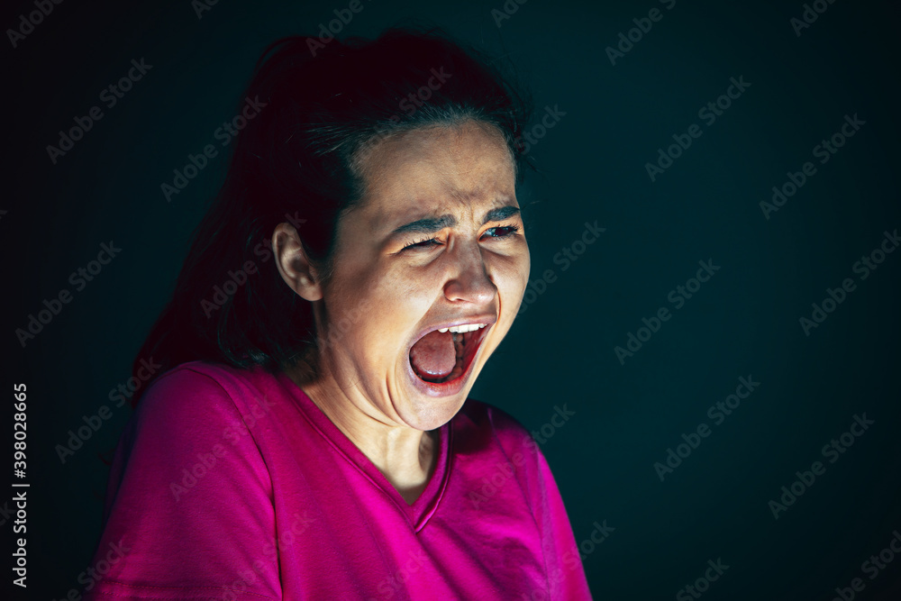 Fototapeta premium Screaming. Portrait of young crazy scared and shocked caucasian woman isolated on dark background. Copyspace for ad. Bright facial expression, human emotions concept. Looking horror on TV, cinema.